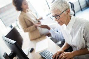 Woman in white collared shirt typing at a work computer